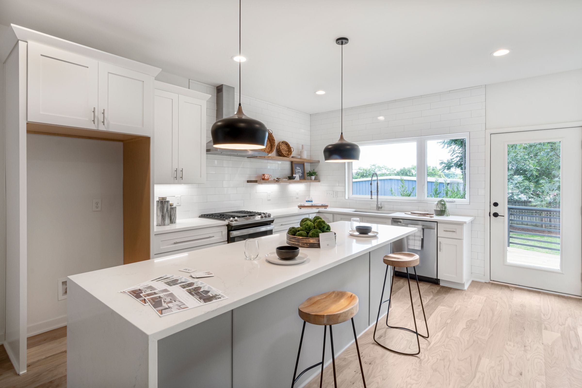 Remodeled kitchen with white shaker cabinets, a quartz waterfall island and black pendant lights